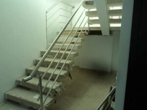 Escalera interior de diseño moderno con escalones protegidos, viga central de soporte y barandilla tubular metálica inclinada.