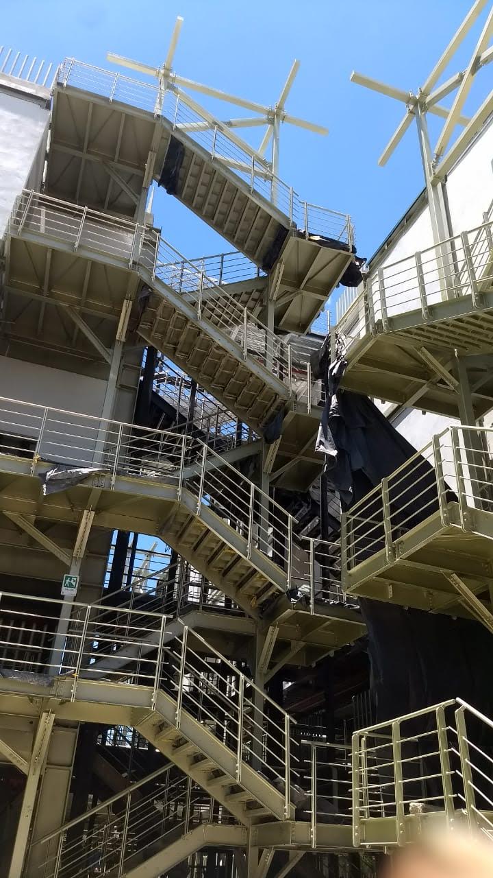 Vista exterior en contrapicado de una edificación con una compleja red de estructuras metálicas, escaleras de evacuación y pasamanos bajo un cielo despejado.