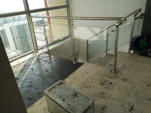 Vista superior de un descanso de escalera con paneles de vidrio templado sujetos por soportes de acero inoxidable y un gran ventanal al fondo con vista a la ciudad.