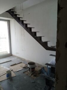 Vista lateral de una estructura metálica para escalera interior con soportes en forma de dientes de sierra sobre una pared blanca.