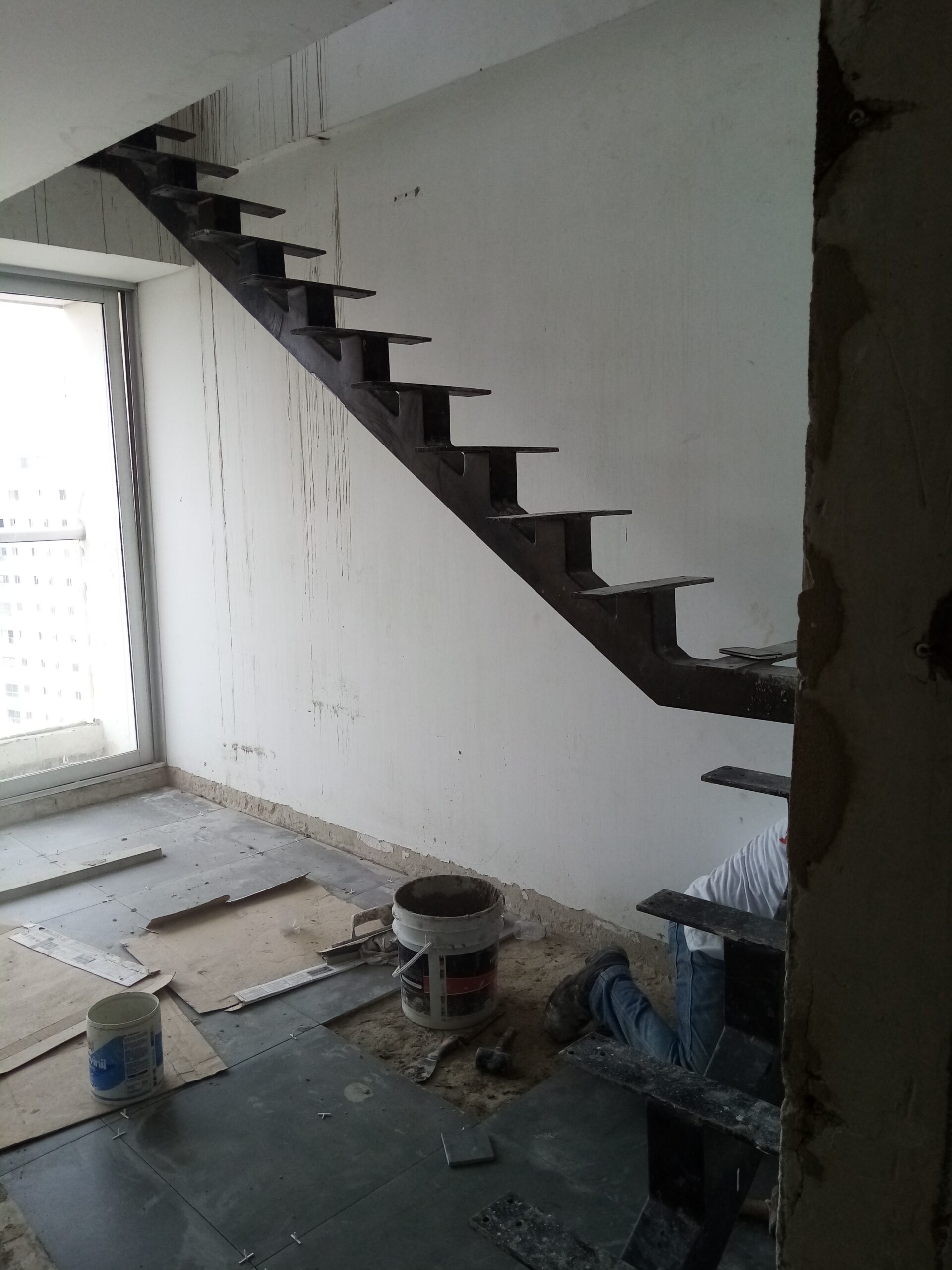 Vista lateral de una estructura metálica para escalera interior con soportes en forma de dientes de sierra sobre una pared blanca.