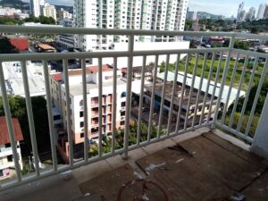 Vista elevada a través de una baranda metálica blanca hacia un paisaje urbano con edificios altos y vegetación.
