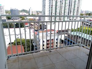 Perspectiva amplia desde un balcón con suelo de baldosas y baranda blanca, mostrando torres de apartamentos y construcciones comerciales en el horizonte.