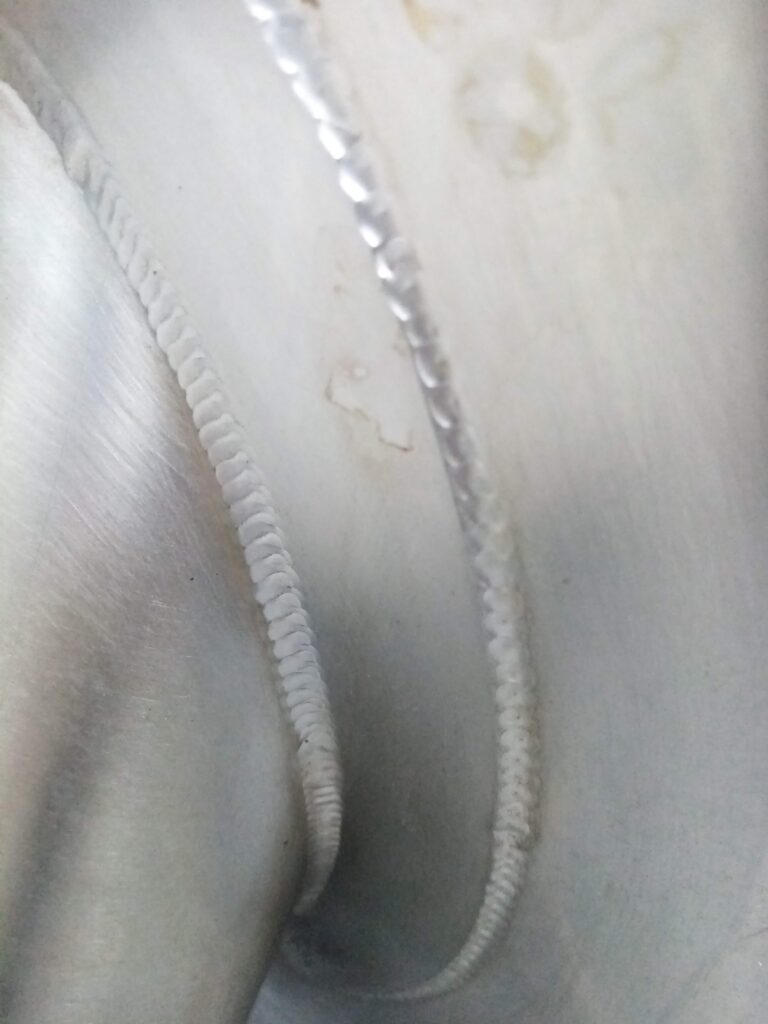 Imagen cercana de uniones soldadas en ángulo sobre superficies metálicas de acero inoxidable, resaltando la precisión del cordón en relieve.