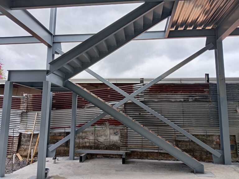 Vista general de una estructura de vigas de acero de varios niveles que integra una escalera diagonal y contravientos en cruz.