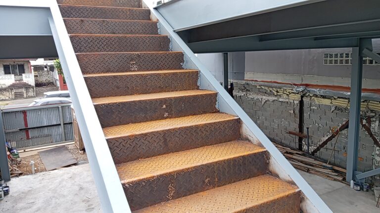 Vista en ángulo ascendente de los escalones de chapa estriada con acabado lateral soldado en una estructura metálica de obra.