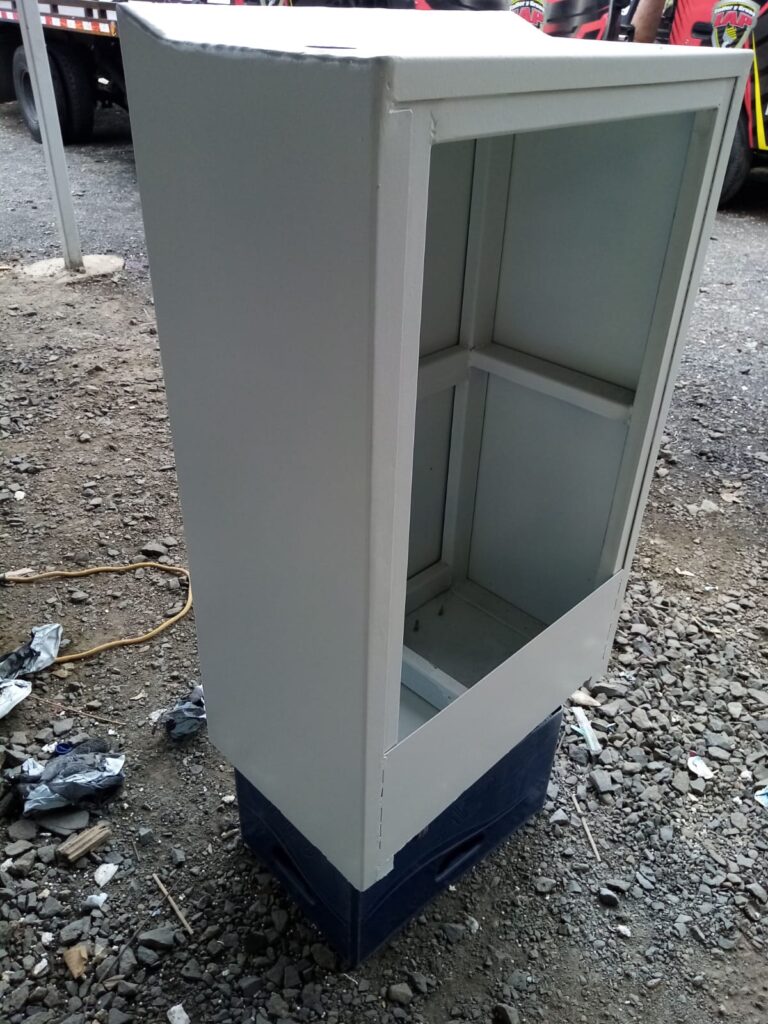 Gabinete de control eléctrico de acero pintado de gris claro sobre una base de plástico azul en un patio de servicio en Panamá, listo para su instalación y soldadura final.