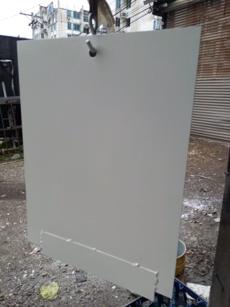 Panel de acero rectangular pintado de gris claro colgando de un gancho en Panamá, mostrando un cordón de soldadura limpio y continuo en la base.
