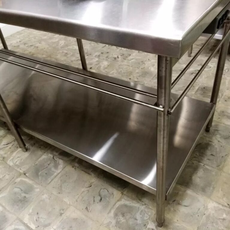 Vista detallada de una mesa de preparación de alimentos de acero inoxidable con superficie lisa, una repisa inferior y barras laterales de soporte.