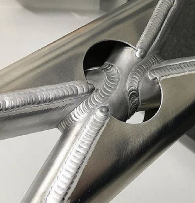 Primer plano macro de uniones soldadas con técnica TIG en tubos de acero inoxidable, mostrando cordones de soldadura limpios, uniformes y en forma de escamas.