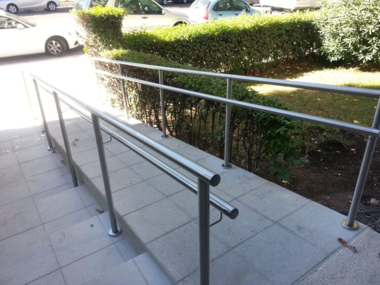 Vista descendente de una rampa accesible y escalones exteriores equipados con pasamanos dobles de tubos de acero inoxidable modernos.