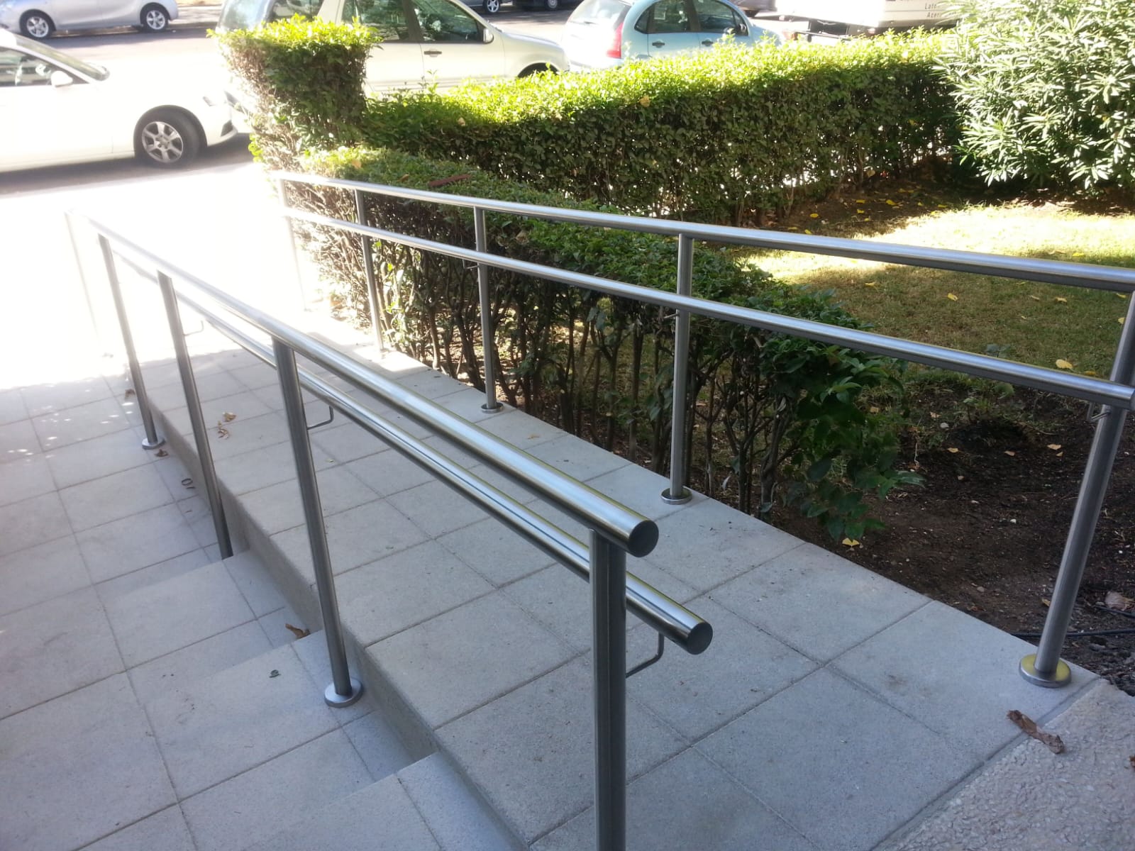 Vista descendente de una rampa accesible y escalones exteriores equipados con pasamanos dobles de tubos de acero inoxidable modernos.
