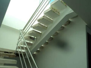 Vista lateral ascendente de una escalera interior moderna con zancas metálicas pintadas de blanco y escalones protegidos con cartón.