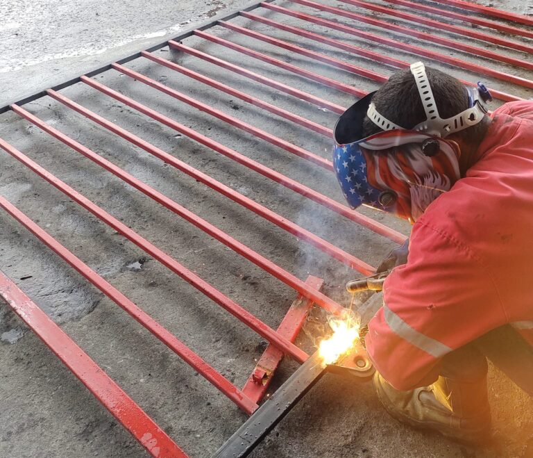 Herrero profesional con máscara de soldar trabajando en el armado de una estructura de portón en el taller.